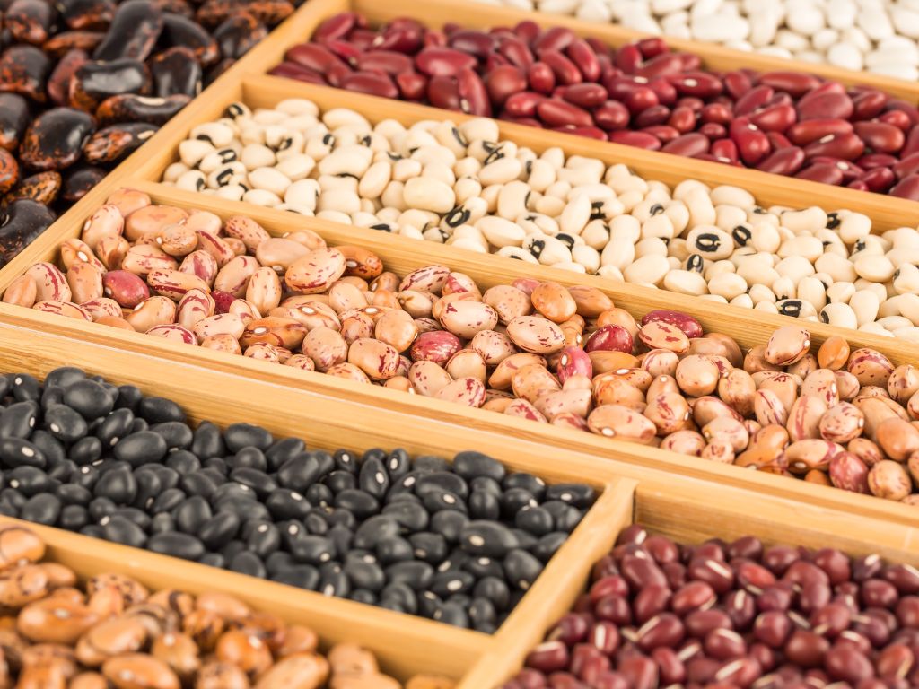 In einem Holzkasten liegen, schwarze, rote, weiße und braune Bohnen.