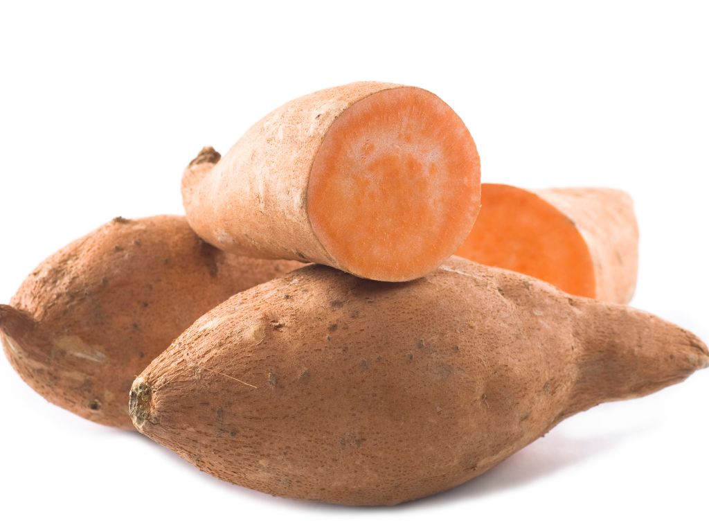 drei Wurzelknollen, eine aufgeschnitten, orange-farbenes Inneres, bräunlich außen