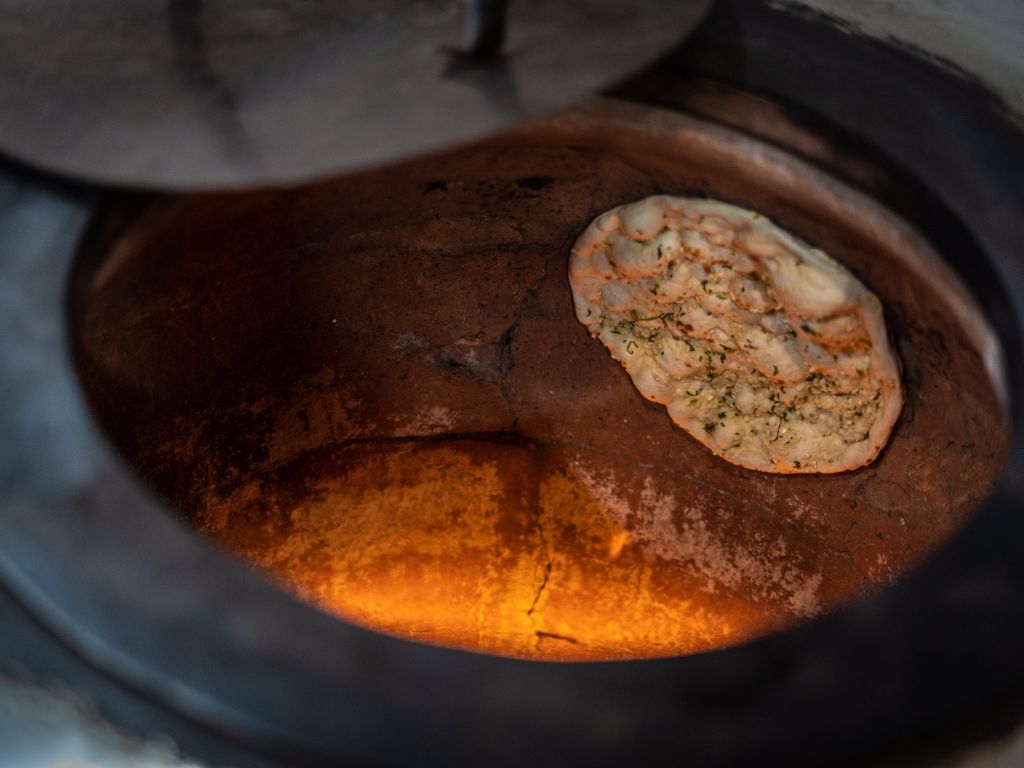 In einem Tandoori Ofen wird ein Roti an der Innenwand des Ofens über offenem Feuer gebacken.