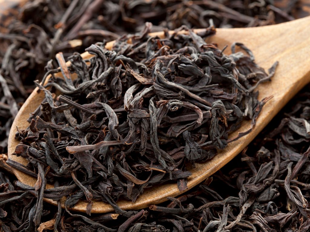 In einem Holzlöffel liegen gekräuselte schwarze Teeblätter.