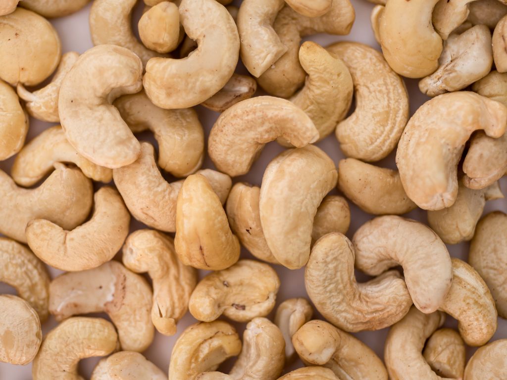 Die geschälten Cashewkerne liegen auf einer weißen Unterfläche.