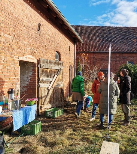 An einem Backsteinhaus stehen vier Personen in warmer Kleidung und besprechen den Arbeitseinsatz.