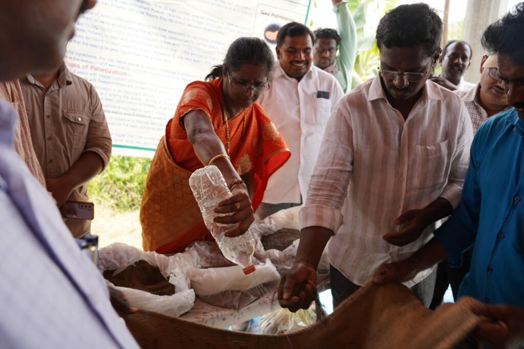 Two men hold a cloth in the air, another adds soil. A woman sprays water on the seeds on the cloth.