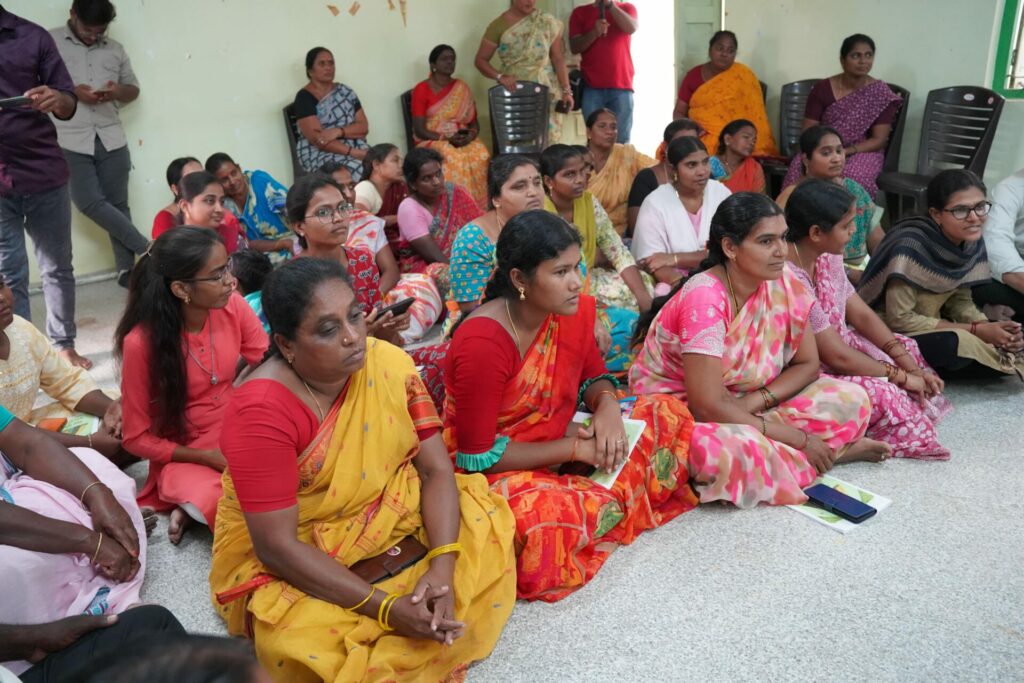A group of Indian women in colorful saris sit on the floor.