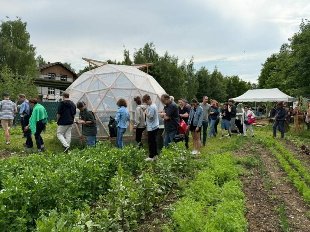 Eine Schlange Menschen geht über den Weltacker, vorbei am Geodom. 