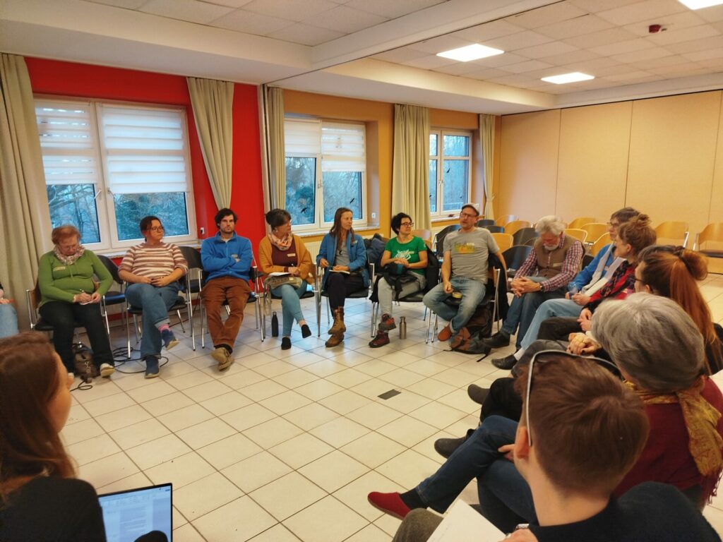 In einem Stuhlkreis sitzen eetwa 20 Personen und diskutieren.